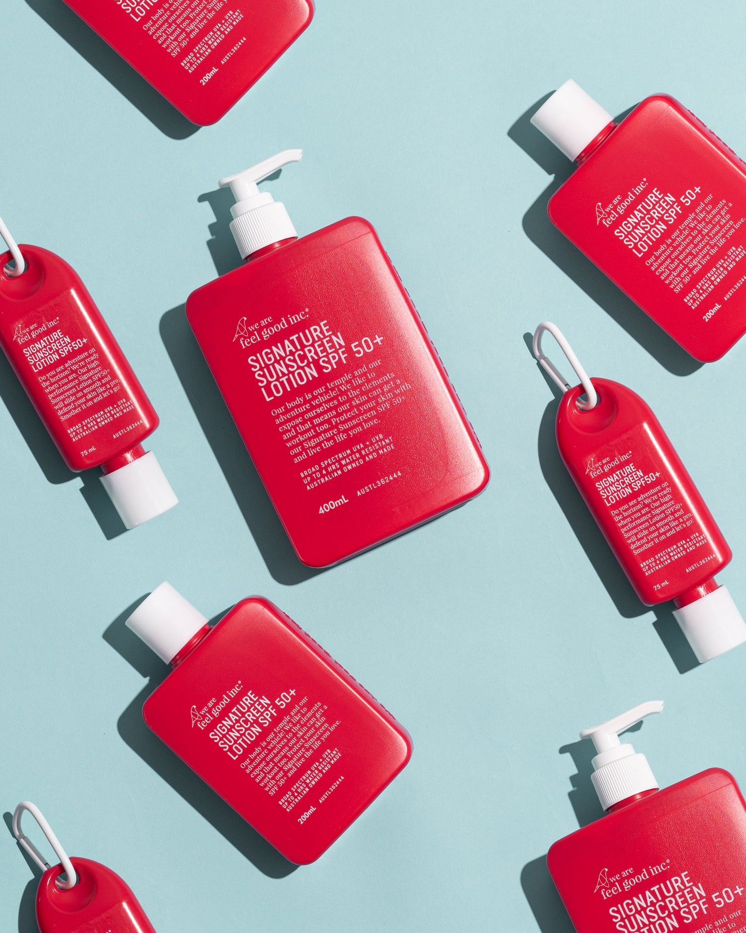Three 200ml red bottles of We Are Feel Good Inc. Signature Sunscreen Lotion SPF 50+ are arranged diagonally