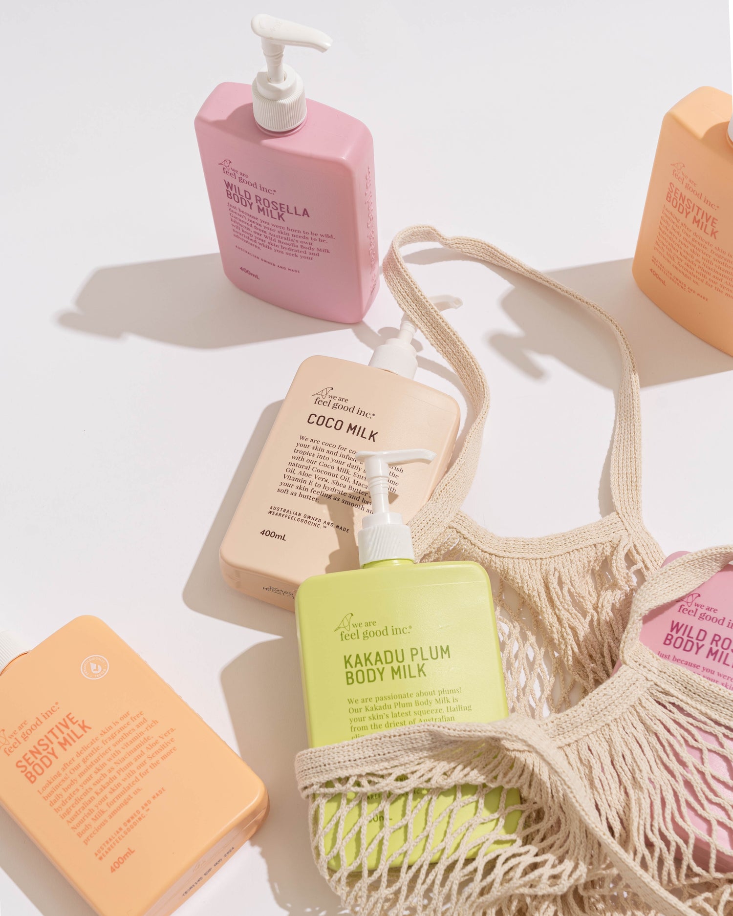 An array of We Are Feel Good Inc. body milk lotions in pink, peach, and beige, with a lime green one in a netted tote bag
