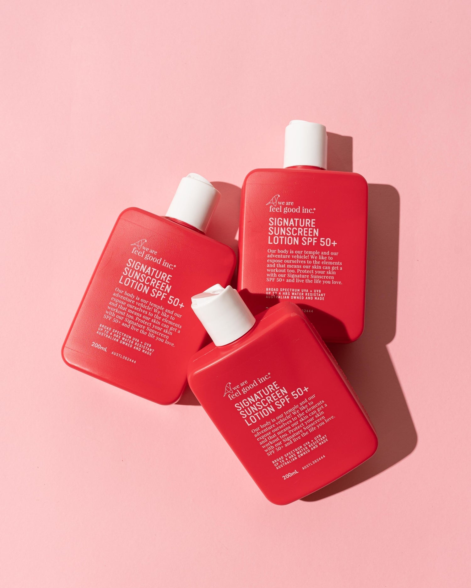 Three 200ml red bottles of We Are Feel Good Inc. Signature Sunscreen Lotion SPF 50+ are arranged diagonally
