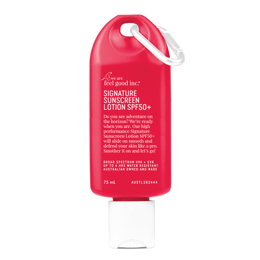 A travel-sized, red 75ml 'We Are Feel Good Inc.' SPF50+ Sigature Sunscreen bottle with a loop on the side for easy carrying