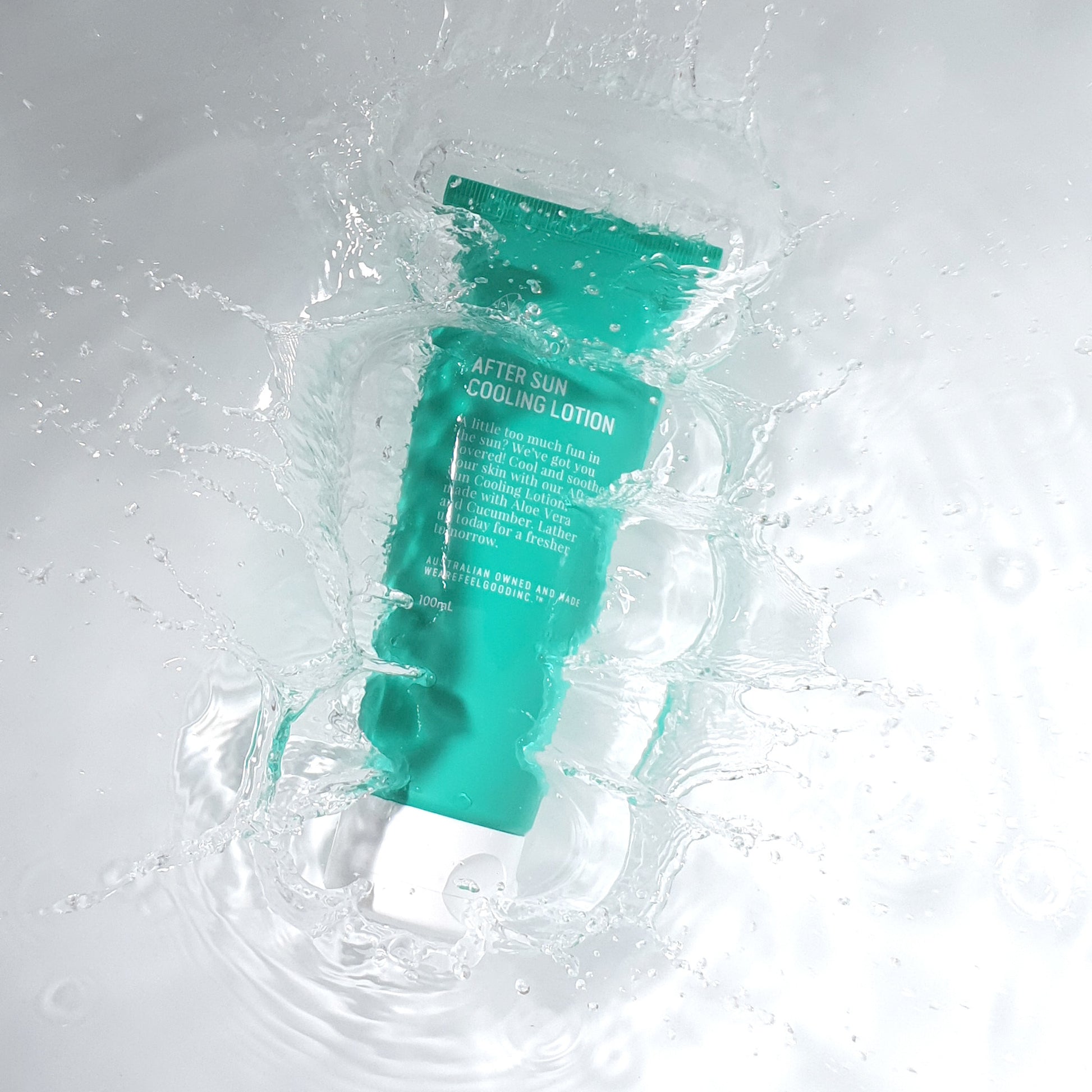 A green tube of 'We Are Feel Good Inc. After Sun Cooling Lotion' submerged in clear water, creating a dynamic splash effect